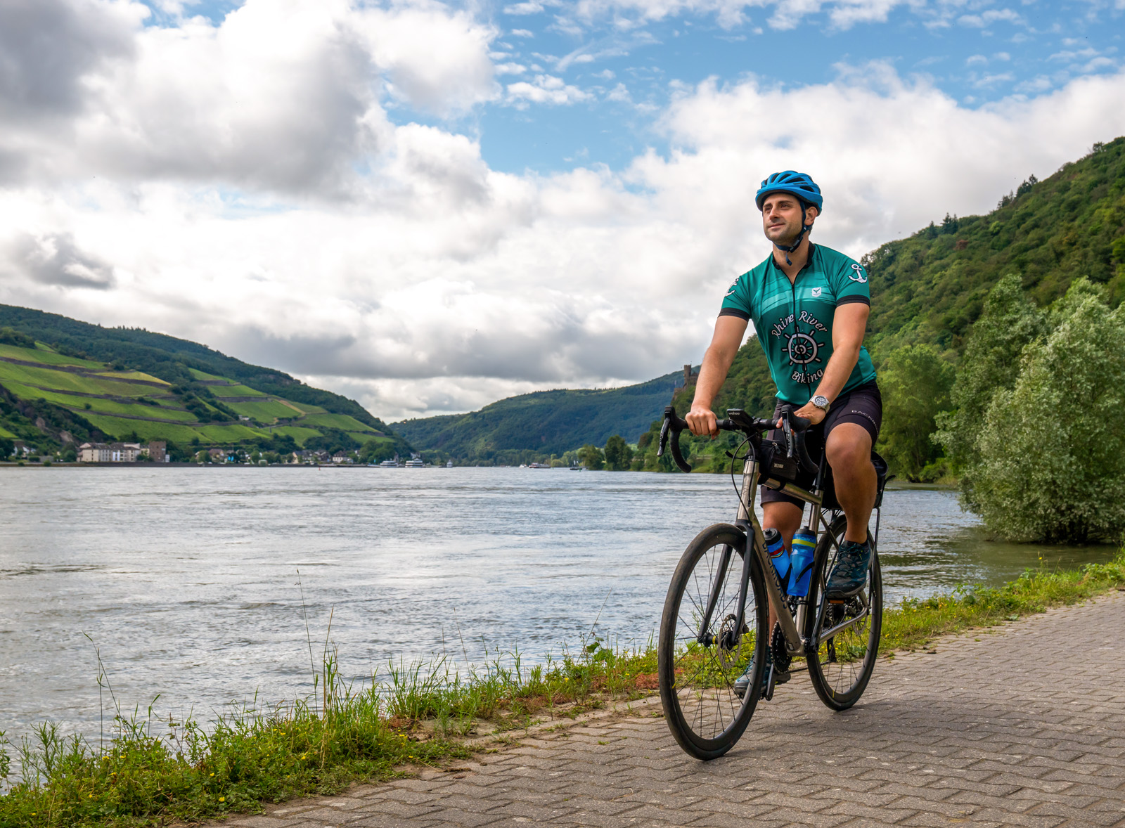 Man riding a bike on a stone path, next to a large lake