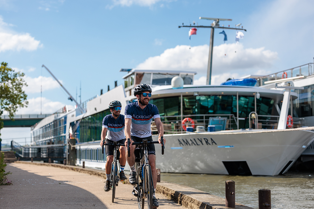 Two cyclists riding by a cruise ship