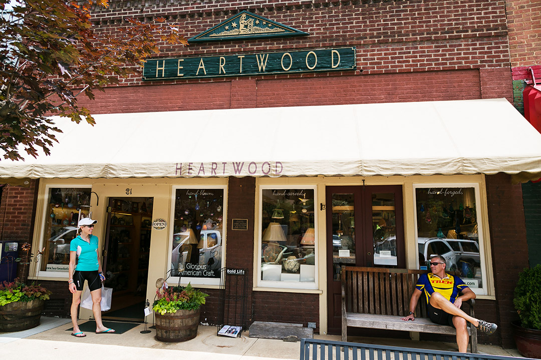 Man sitting on a bench in front of a store with a woman on the left smiling
