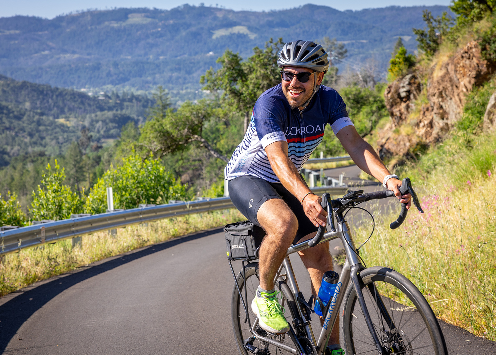 Man wearing biking gear and sunglasses, riding a bike on a hairpin road