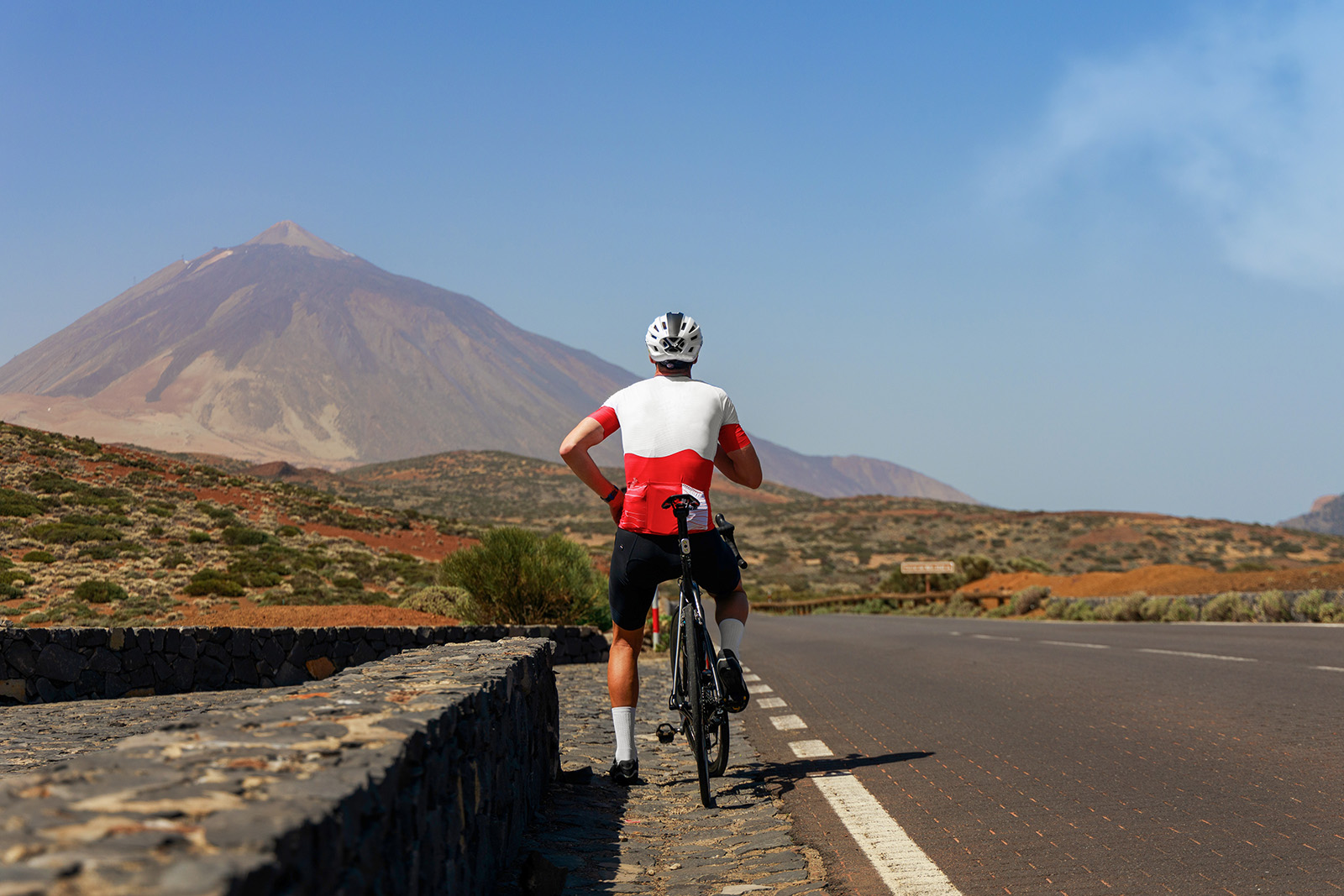 Man in a white and red shirt, riding a bike on a road with mountains in the distance