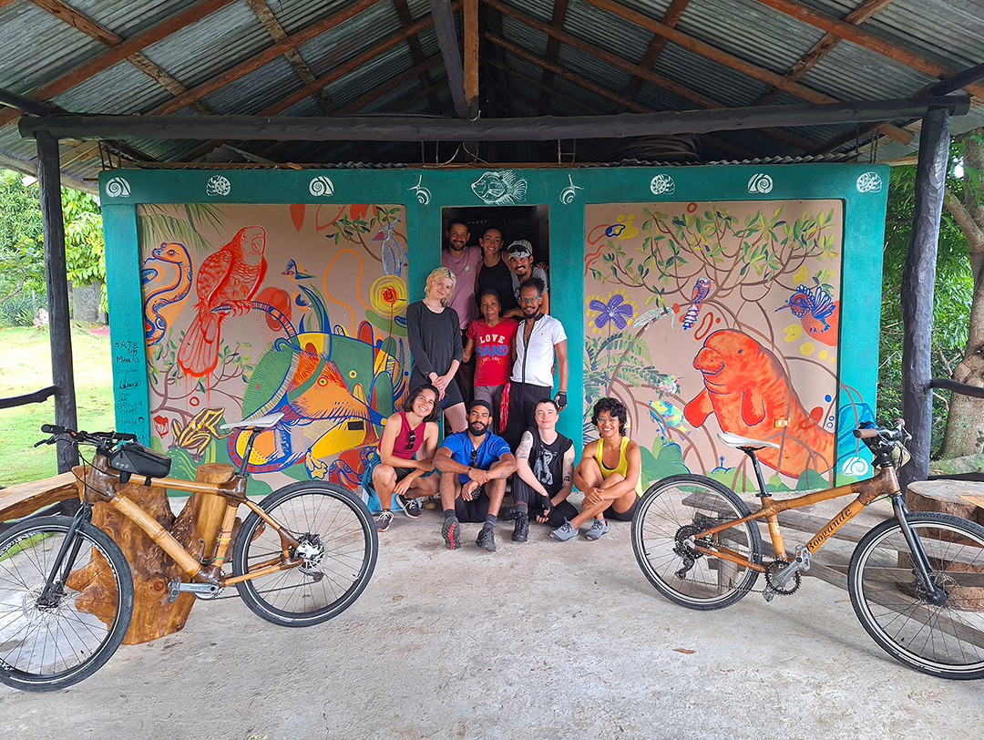 Group of people smiling in front of an art mural with two bikes on either side