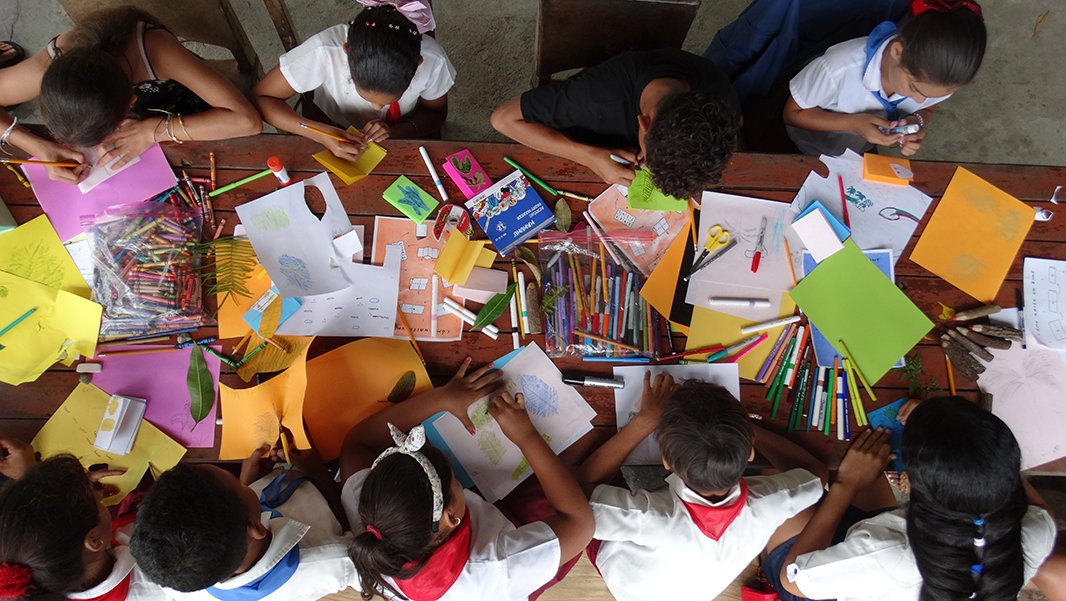 Group of kids sitting at a desk, drawing with coloring pencils on colorful sheets of paper