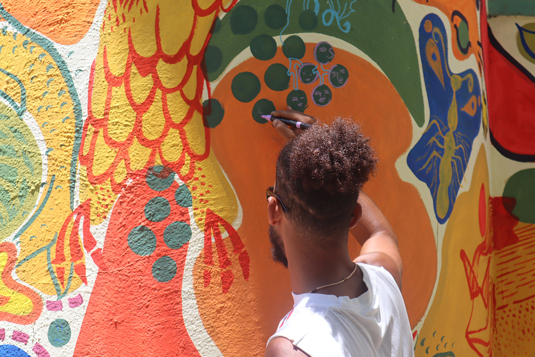 Man drawing on a wall with a larger mural