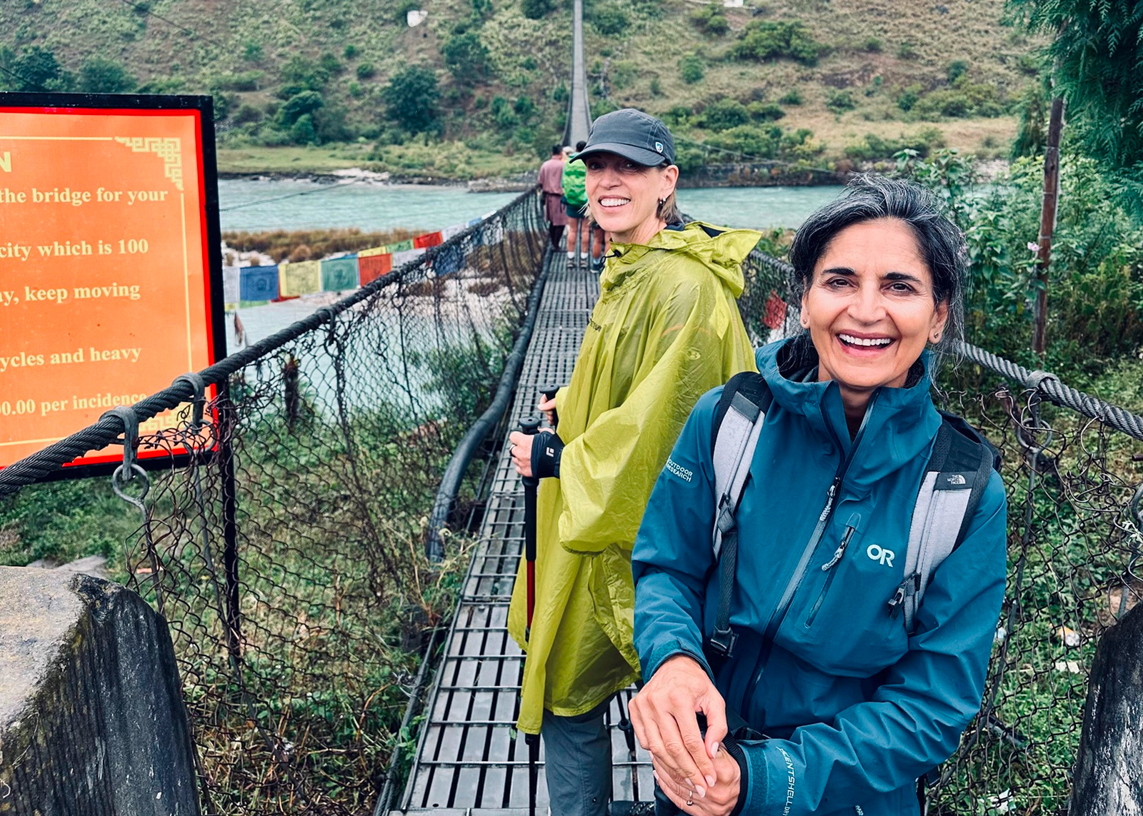 Two women smiling while crossing a wooden bridge over a river