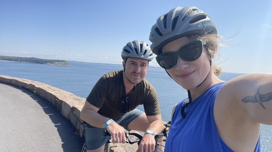 Man and woman wearing biking helmets, smiling in front of the ocean