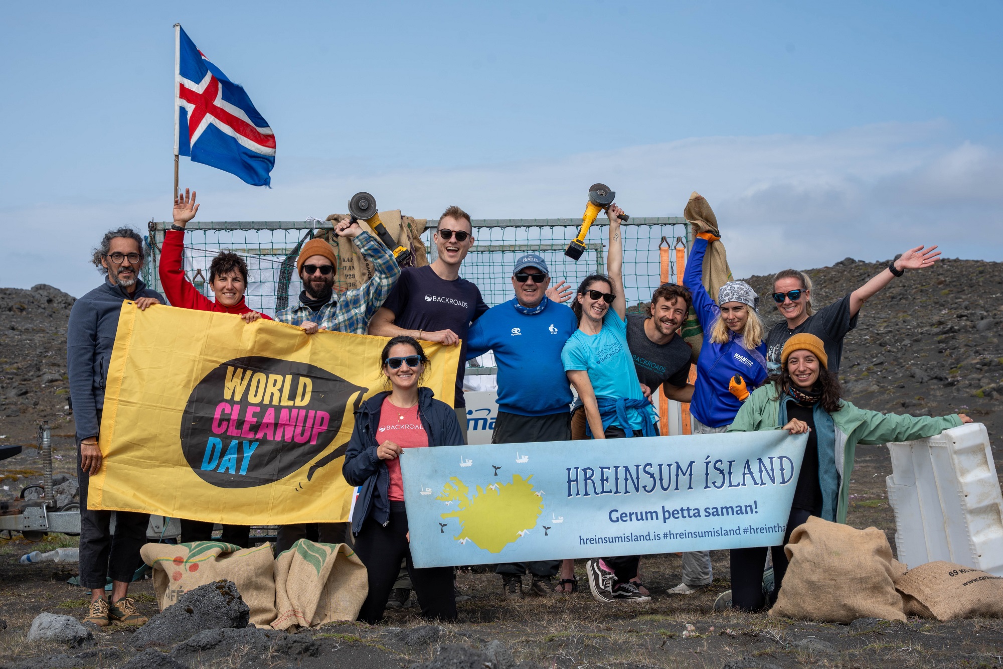 Group of people standing by the ocean, holding up large banners and a flag of Iceland