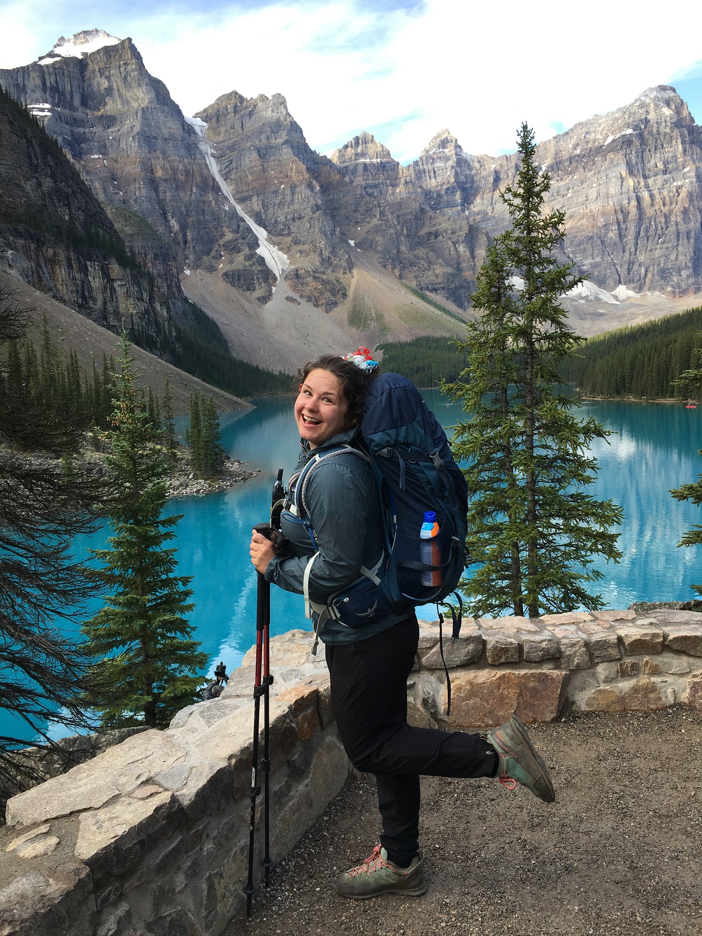 Woman wearing a backpack and holding hiking poles, with a large lake in the background