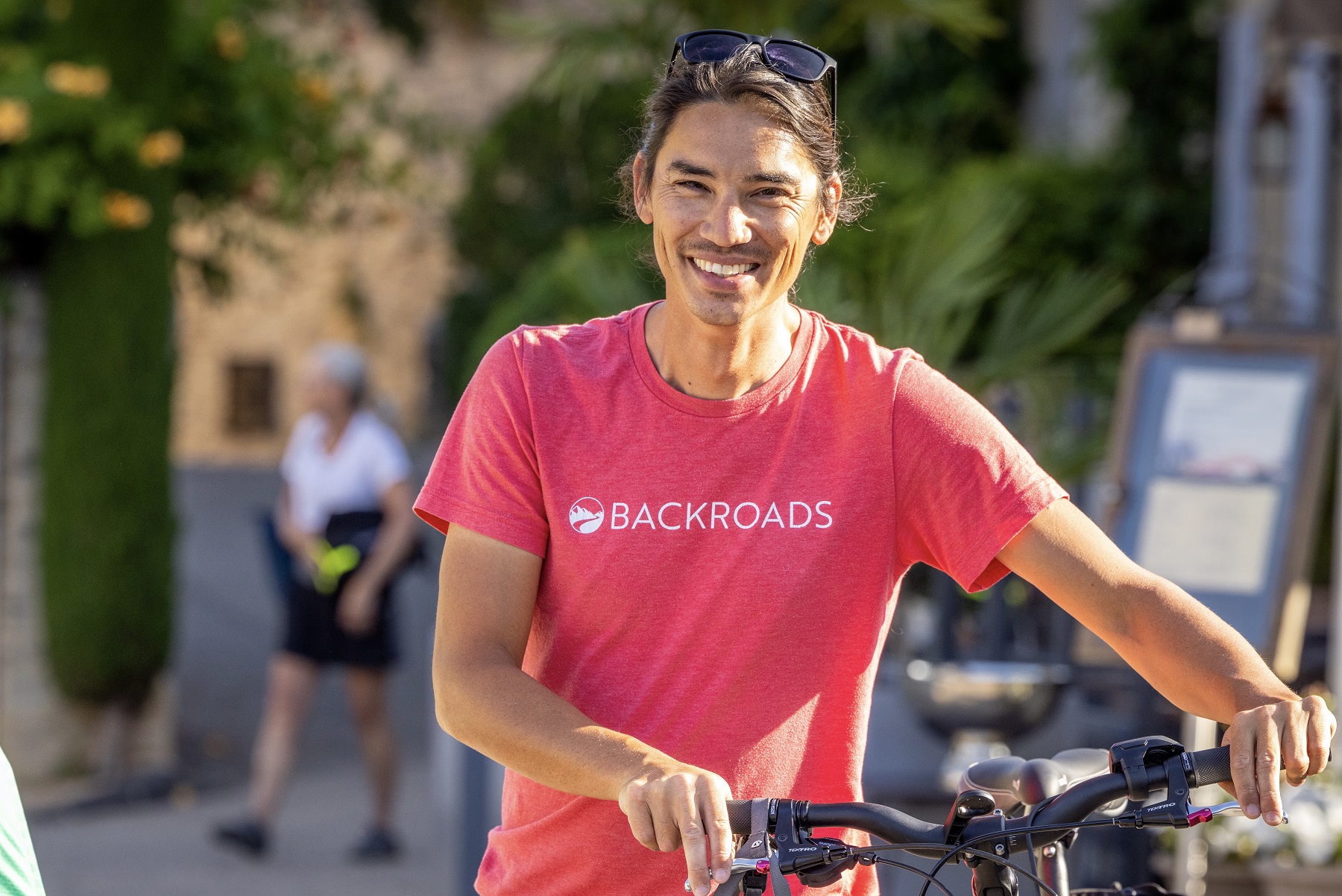 Man with a red shirt, smiling while holding onto a bike
