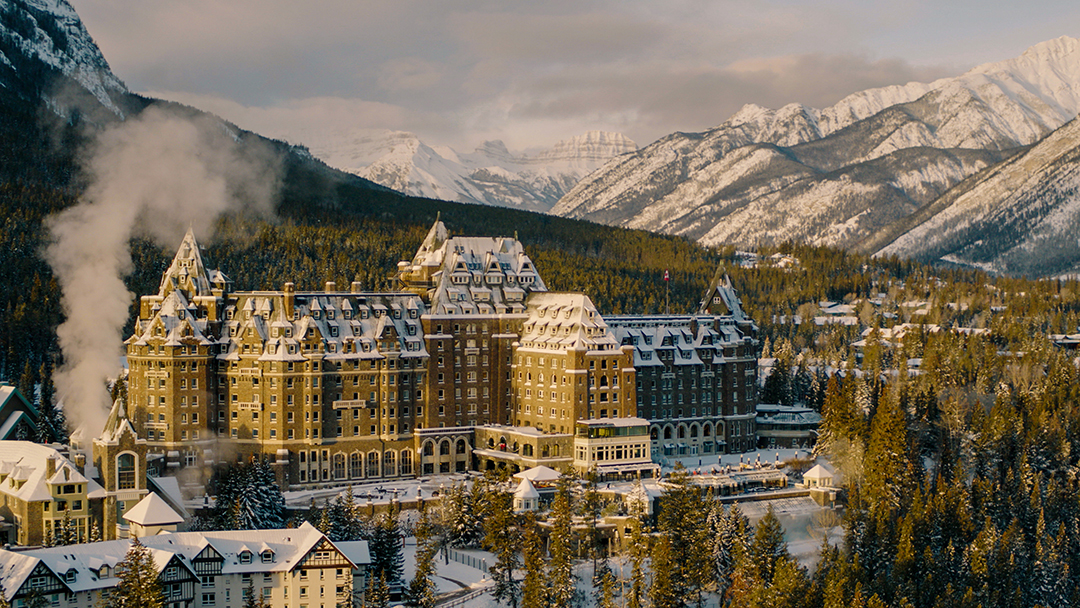 Large, brown hotel building in the middle of a snow and tree-covered valley
