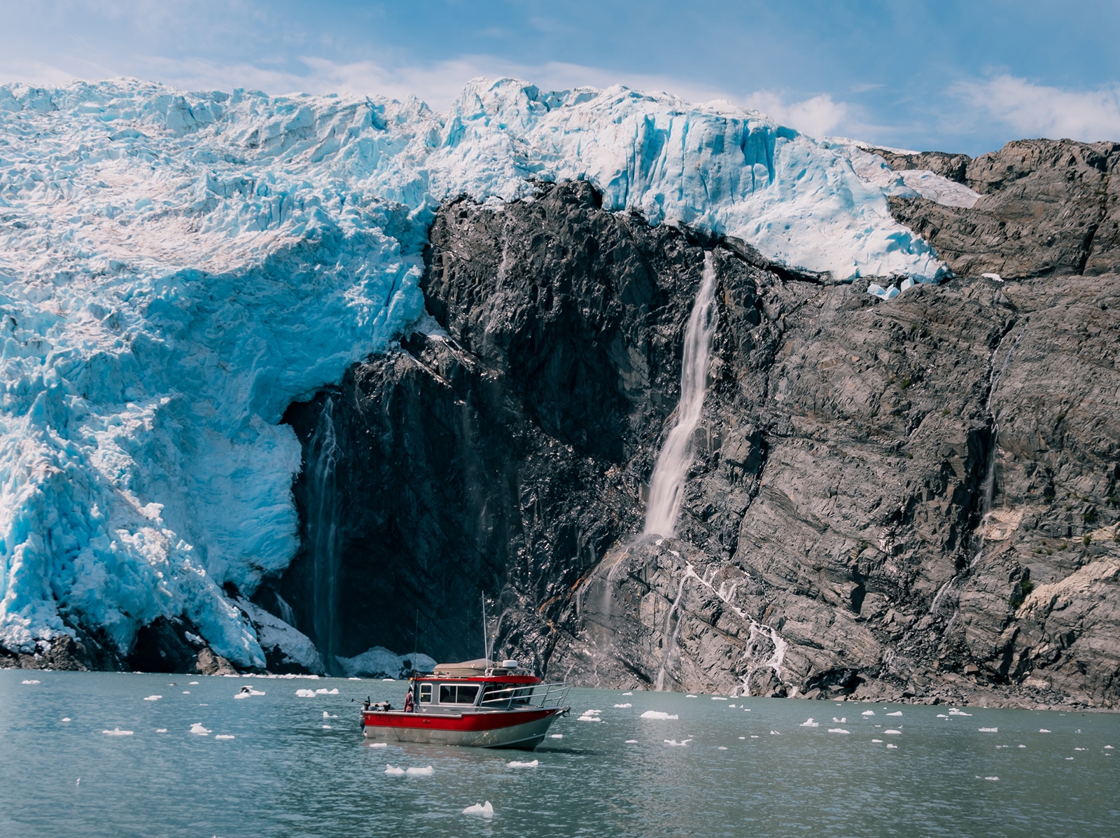 Red and gray boat floating next to large glaciers and cliffs
