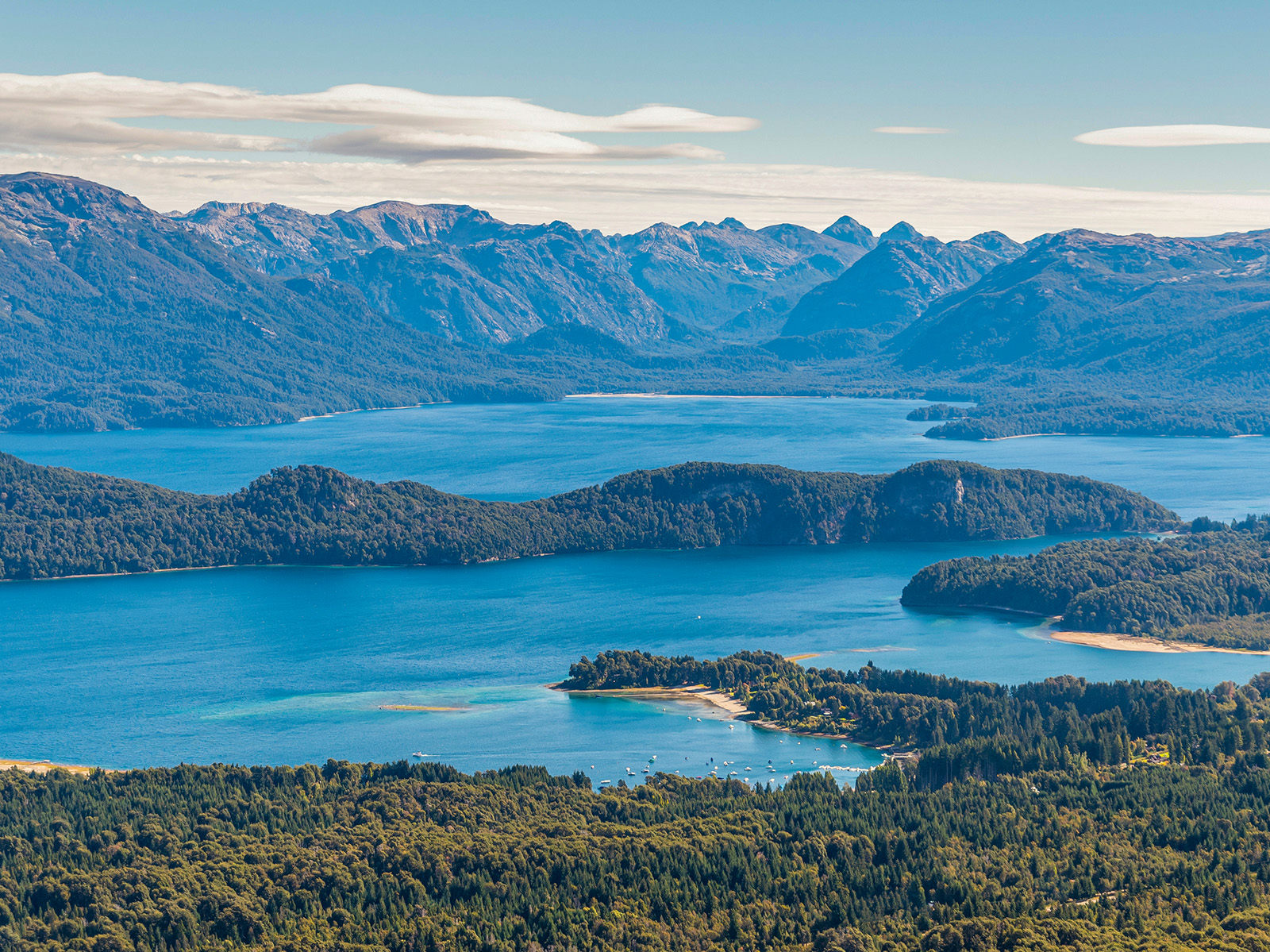 Sky view of a large lake, surrounded by tall mountains and trees
