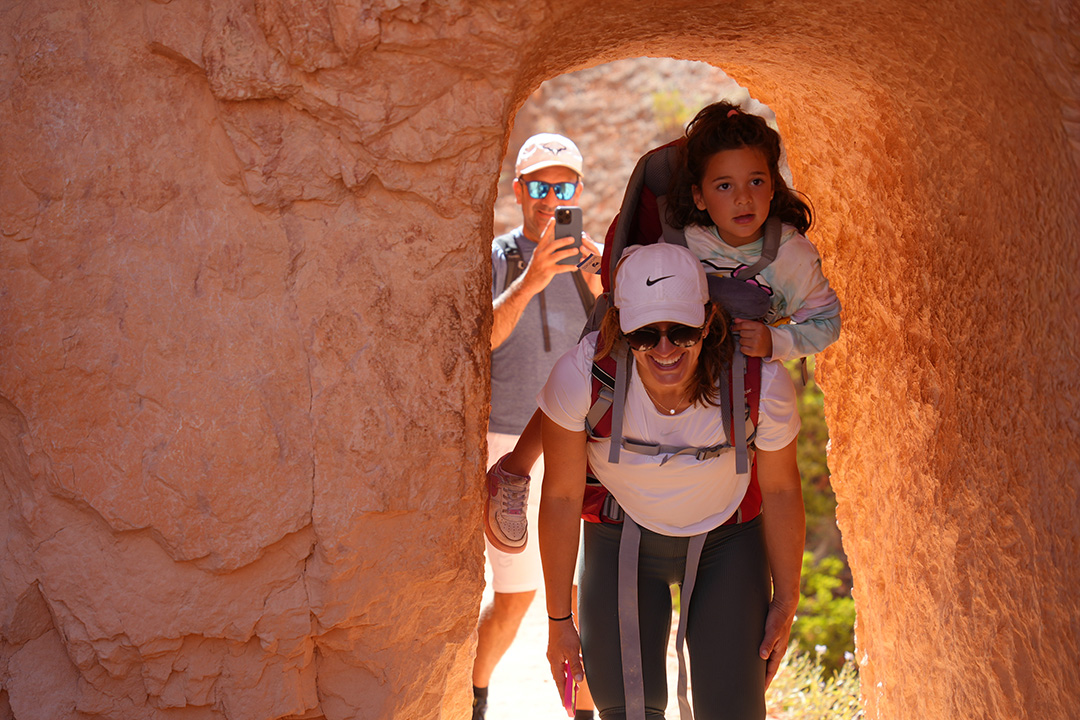 Woman carrying her daughter on her back, walking through an orange canyon