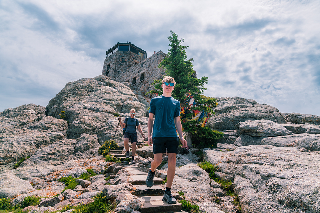 Teenager descending stairs on a rocky cliff, with a stone building at the peak