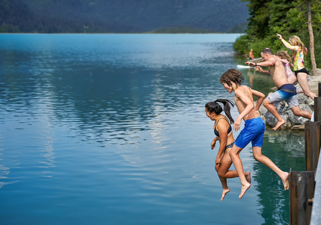 Group of people jumping off a wooden bridge into a large lake