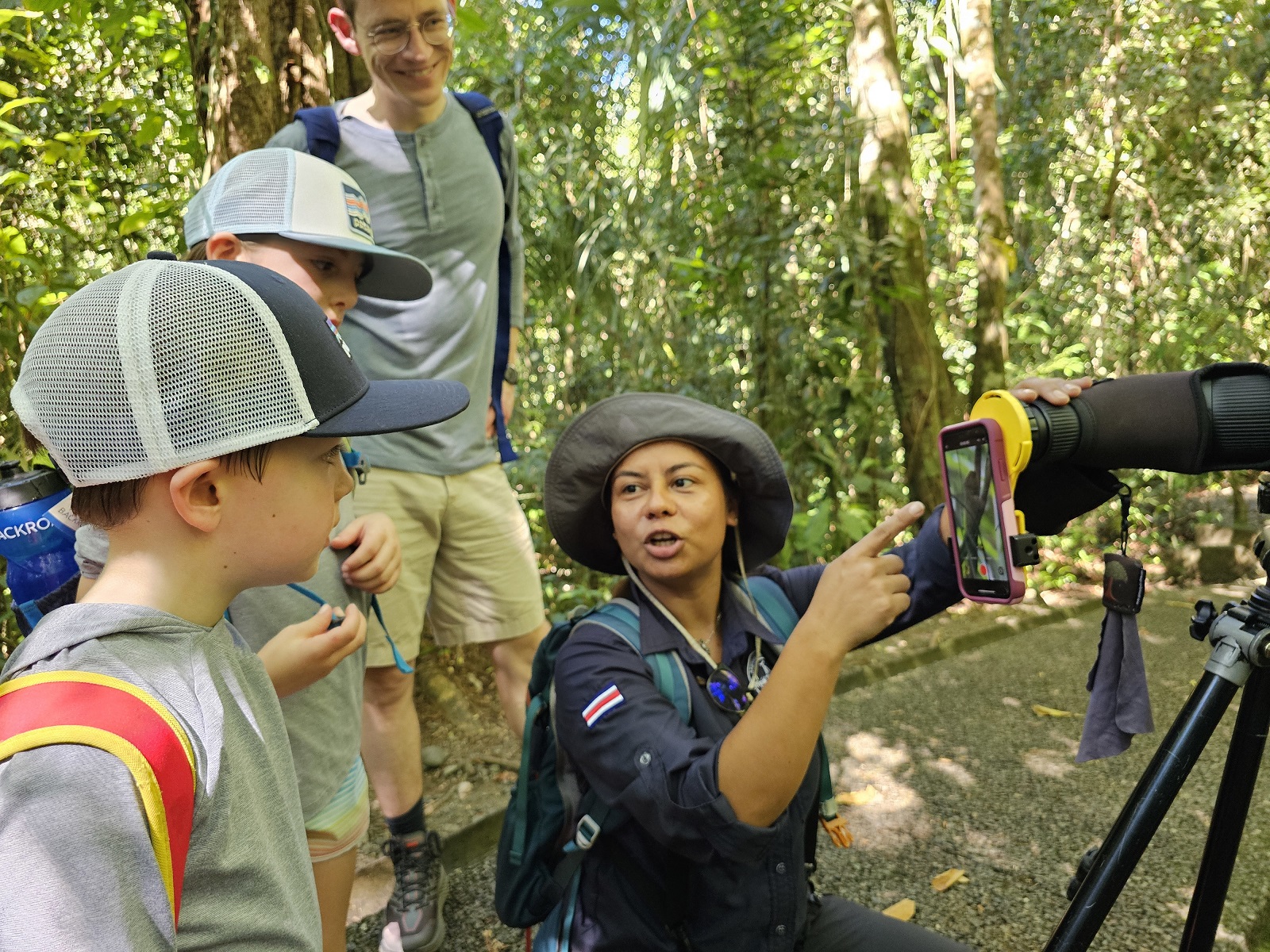 Woman showing a phone to a group of kids in front of a telescope