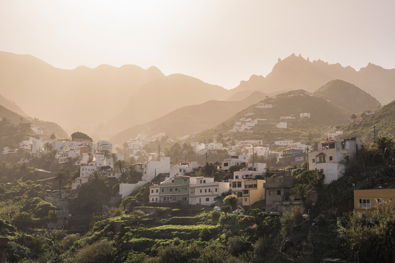 Town of white houses on a grassy hill, with the foggy sunlight in the background