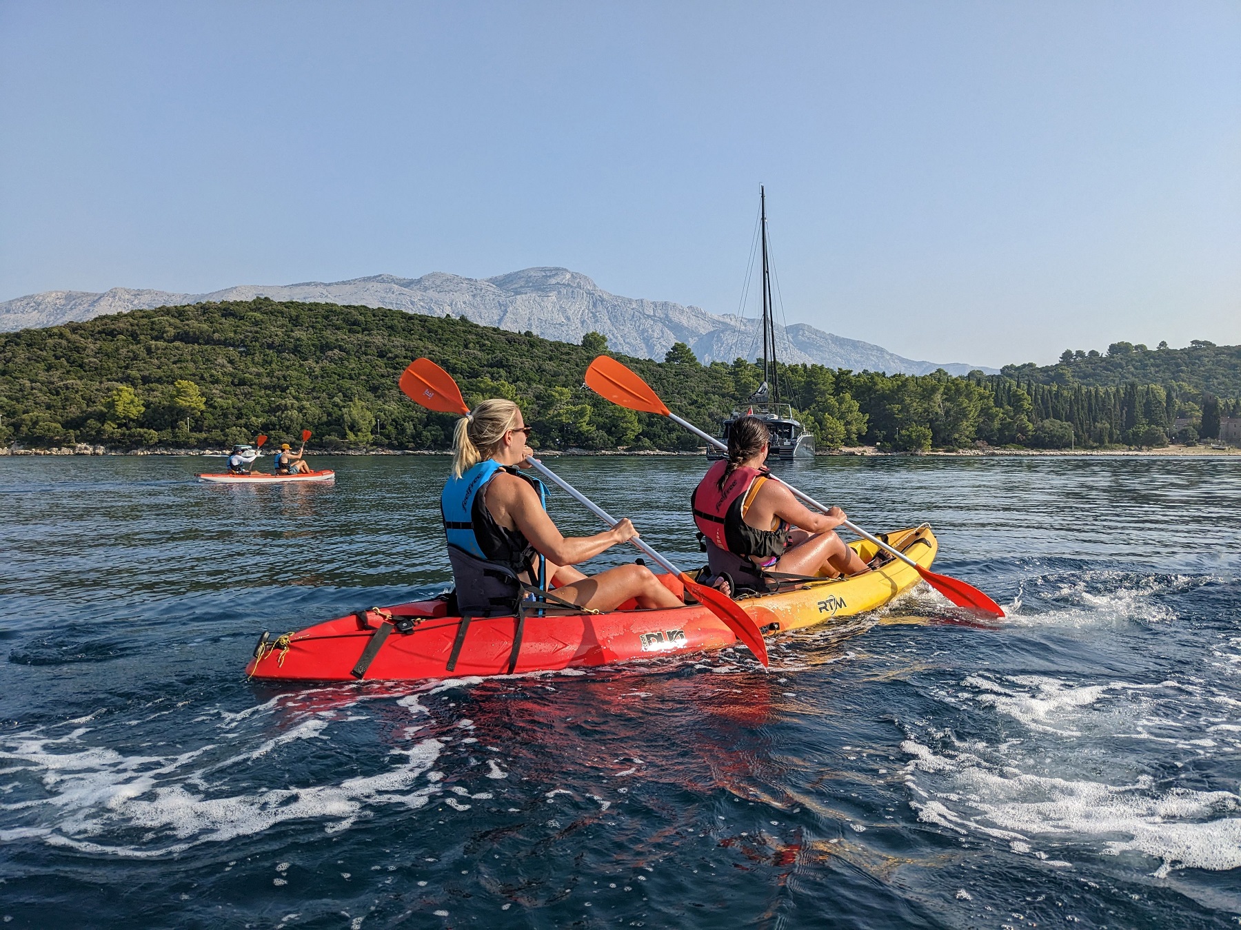 Two women paddling in a red and yellow kayak in the middle of a lake