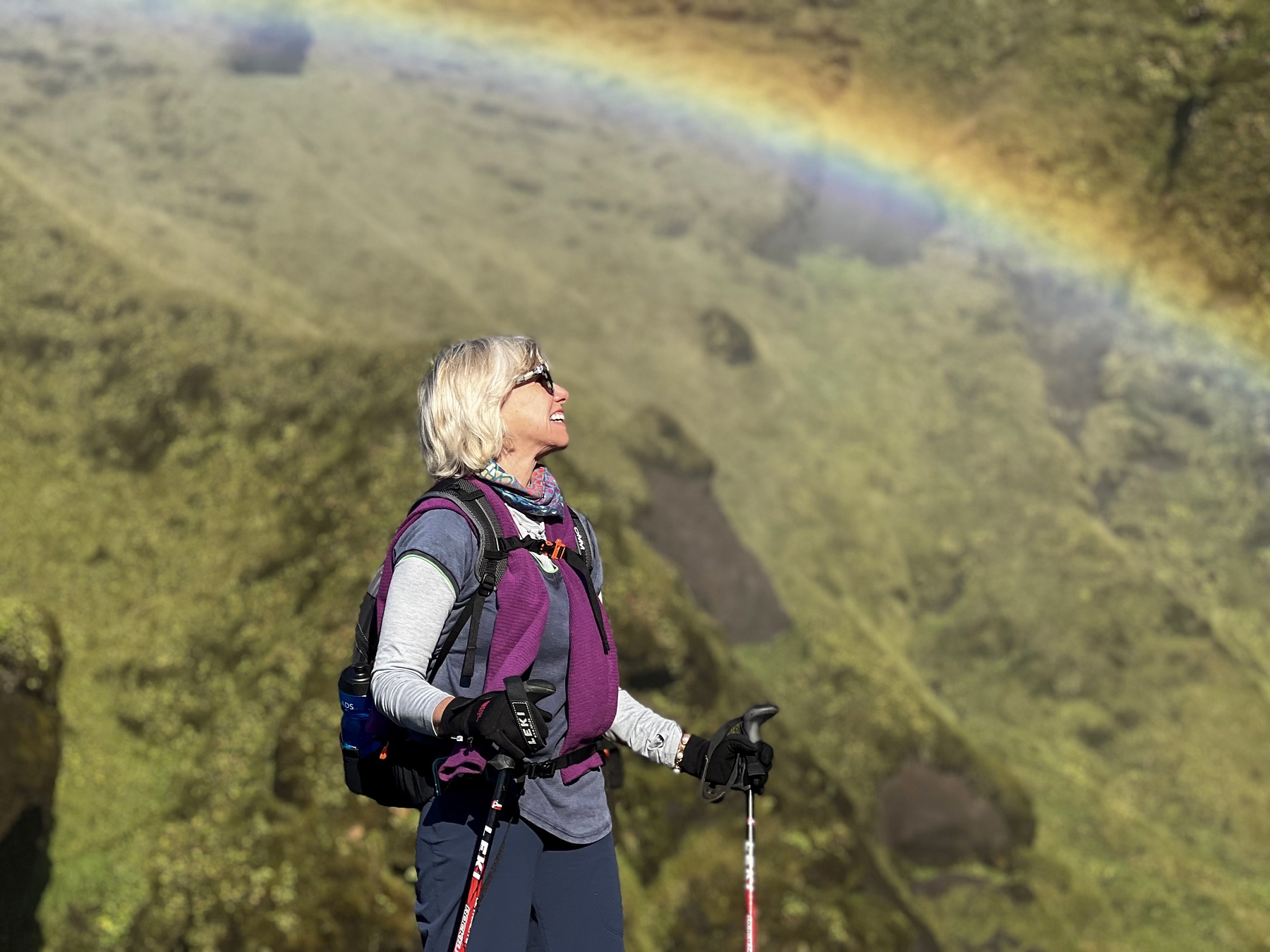 Woman with walking poles looking up to a rainbow