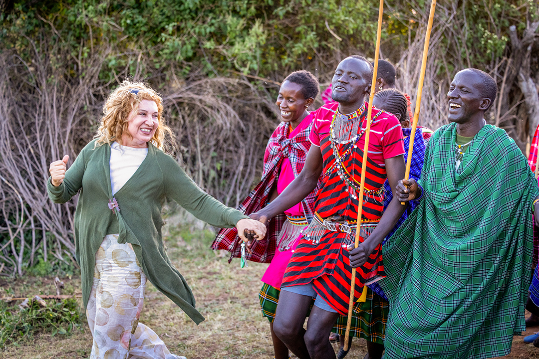 Woman walking along traditionally dressed tribe members, smiling and laughing