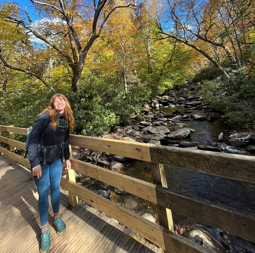 Woman smiling while standing on a wooden bridge on top of a river