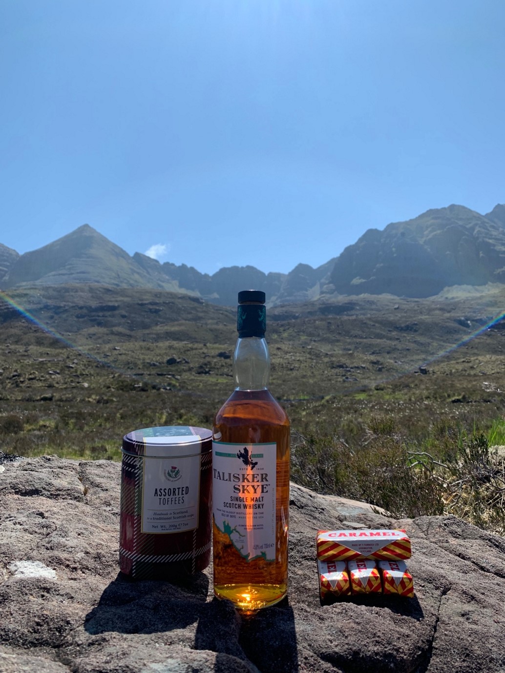 Bottle of whiskey and a can of toffee snacks sitting on a rock