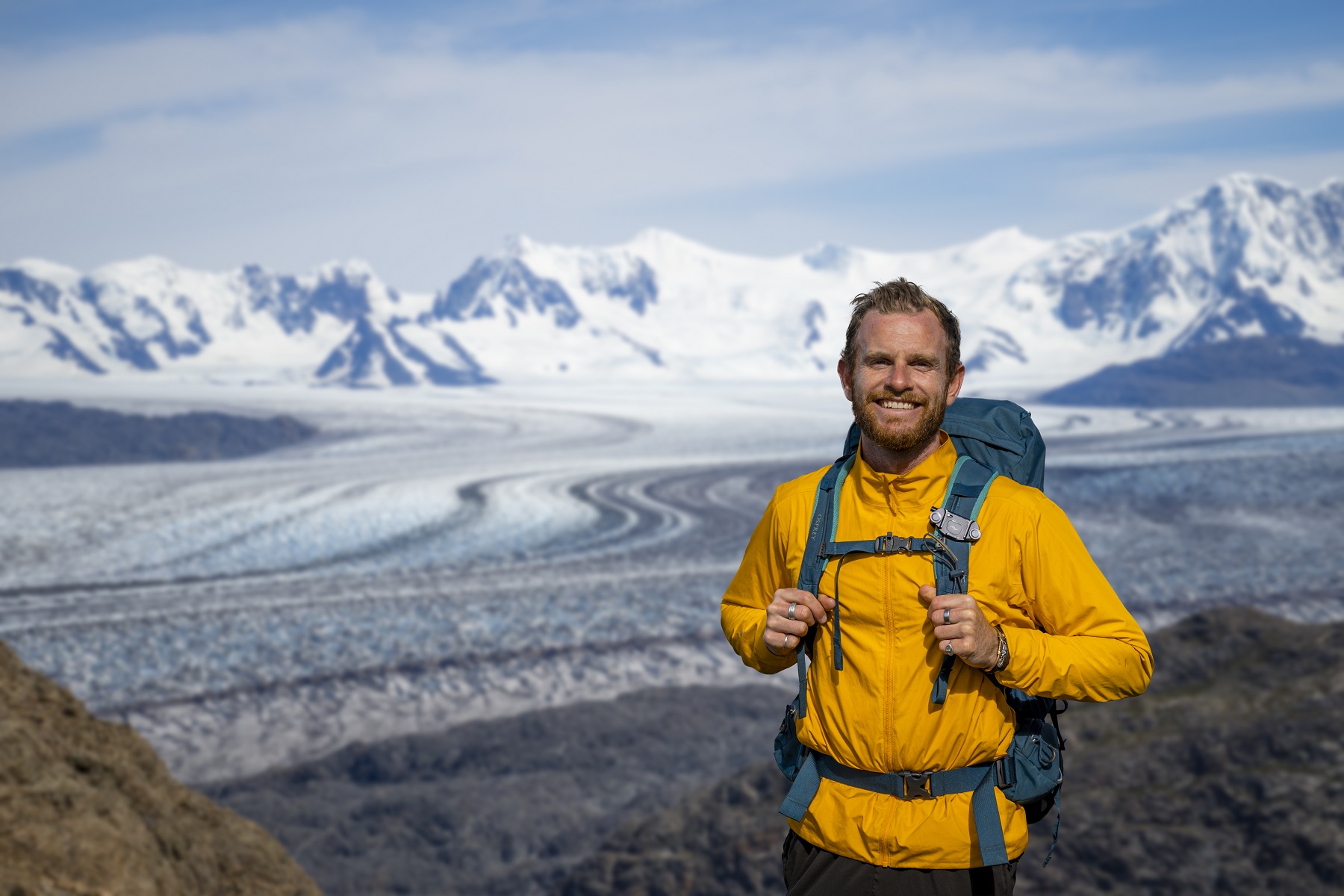Man wearing a yellow jacket, with large mountains in the background