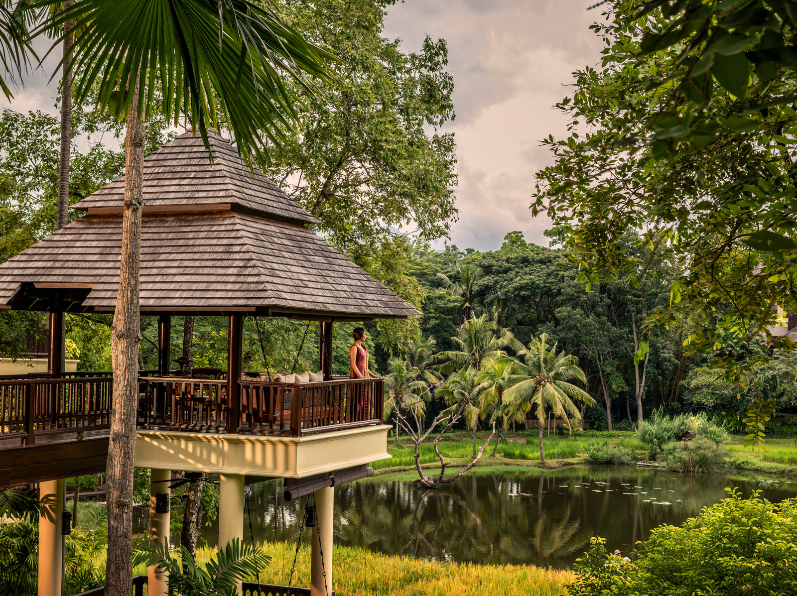 Woman standing on an outdoor patio looking into a jungle and a small lake