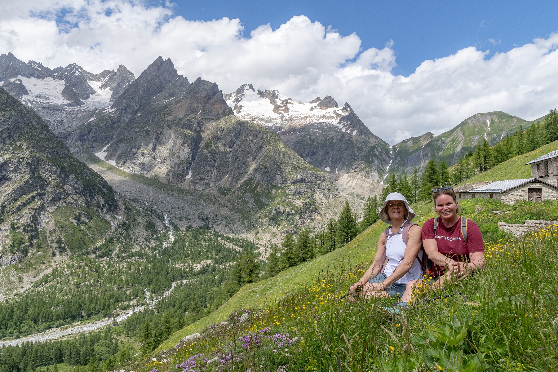 Two women sitting on a grassy hill, with large mountains in the background