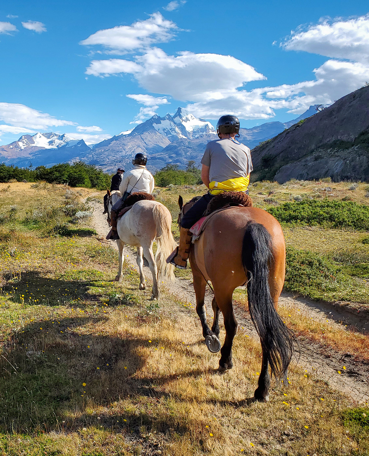 Three people horseback riding on a dirt trail in the middle of an open valley