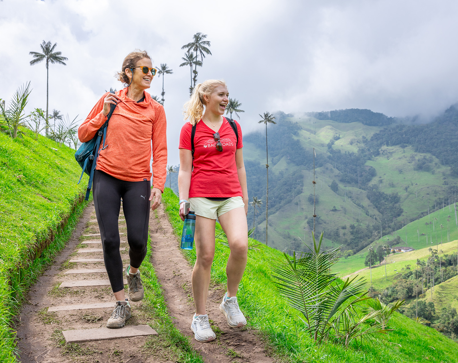 Two women walking on a dirt trail looking out to grassy hills
