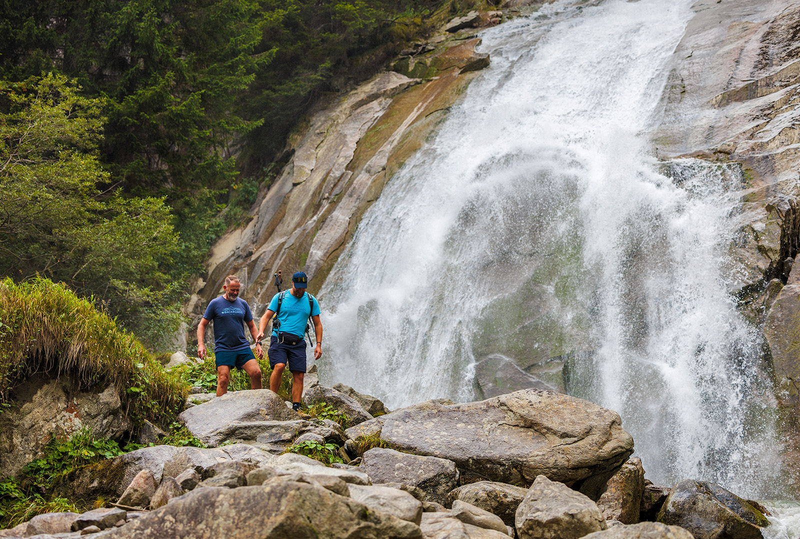 Two men hiking on a rocky trail next to a waterfall