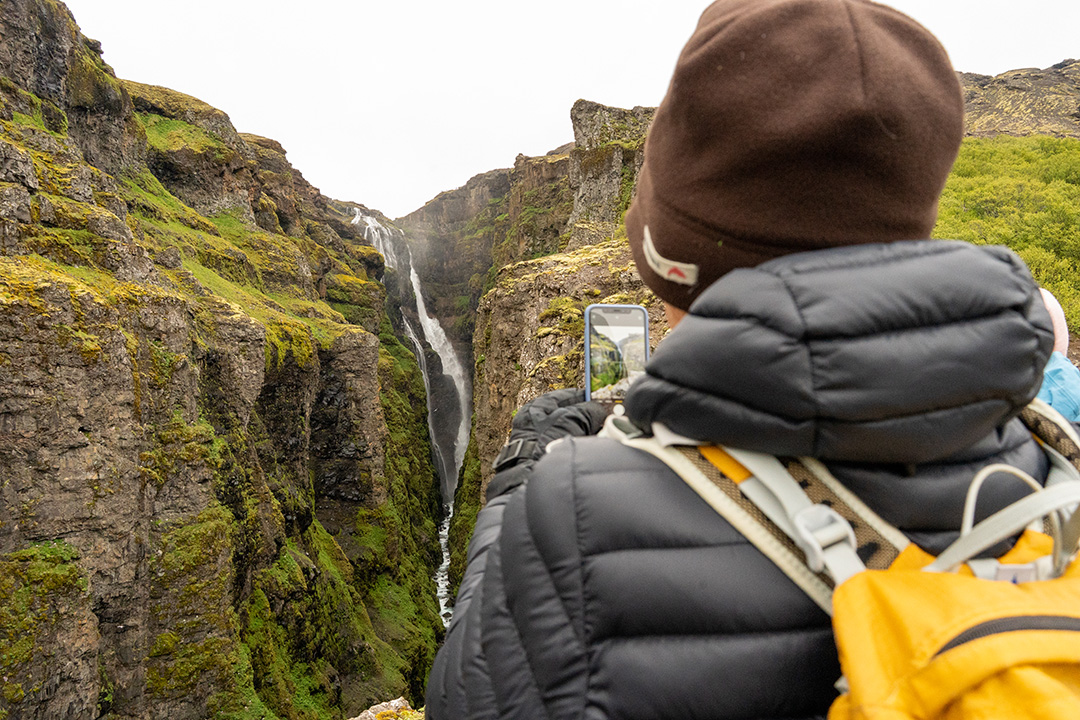 Man taking a photo of a waterfall in between two large cliffs