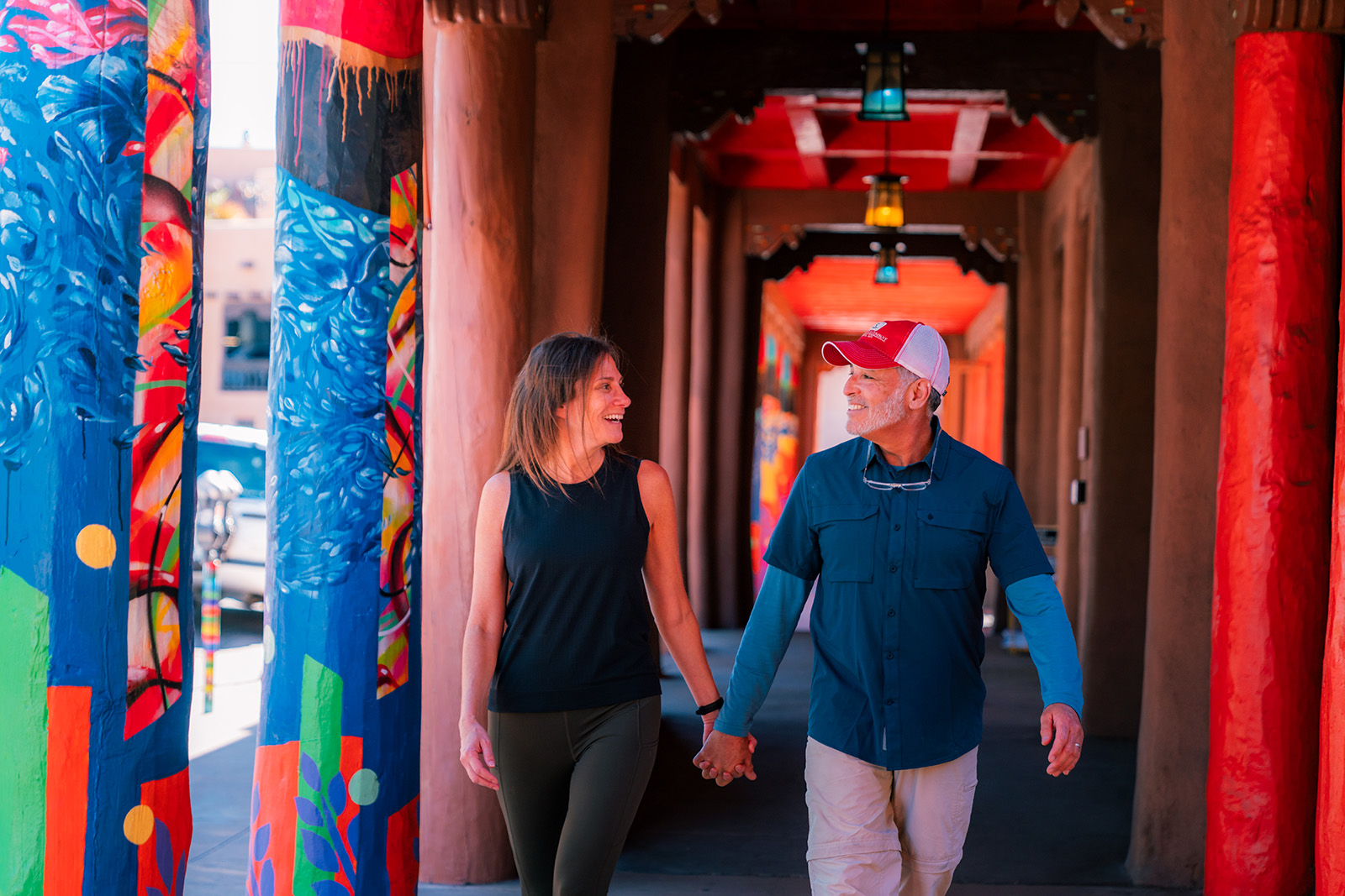 Man and woman holding hands while walking in a colorful passage