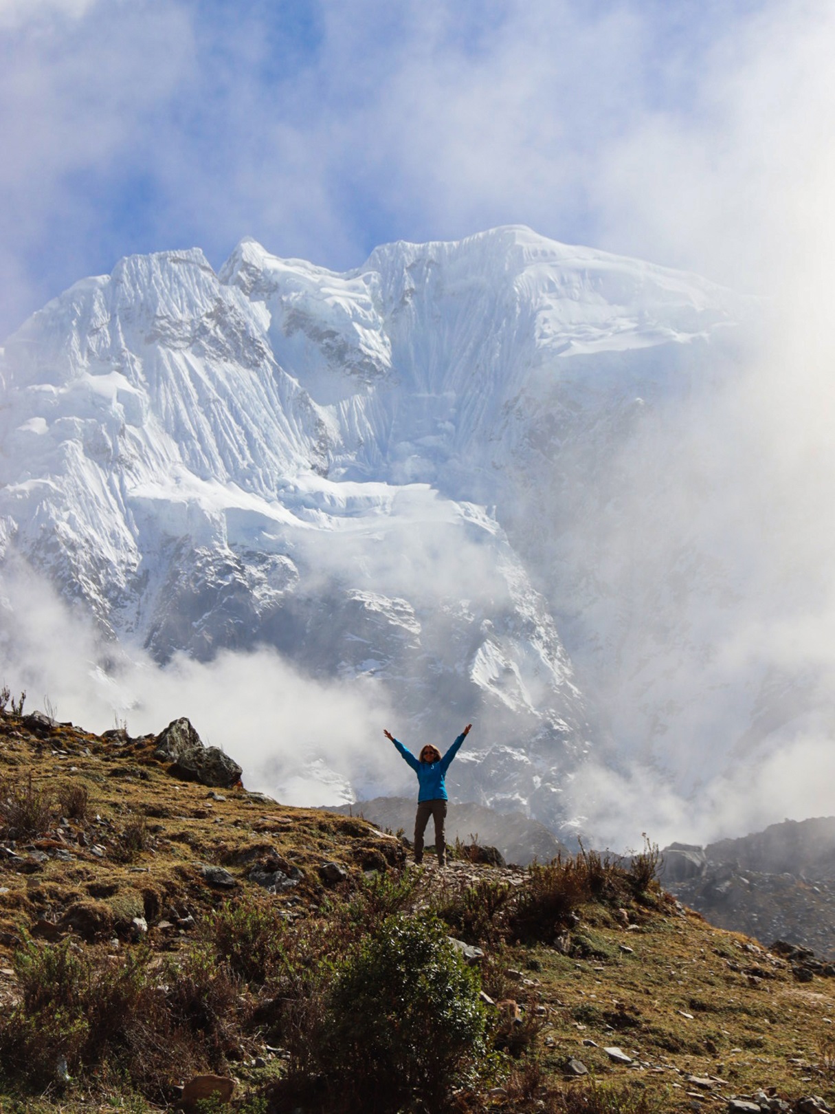 Person standing on top of a cliff with cloudy skies behind