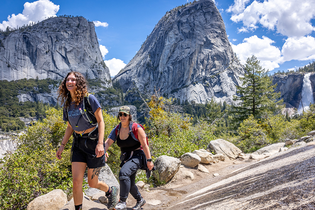 Two women descending a gravel trail with tall mountains in the background