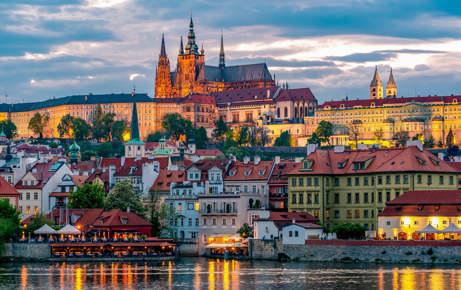 Illuminated European town with a large river in front, and large cathedral in the distance
