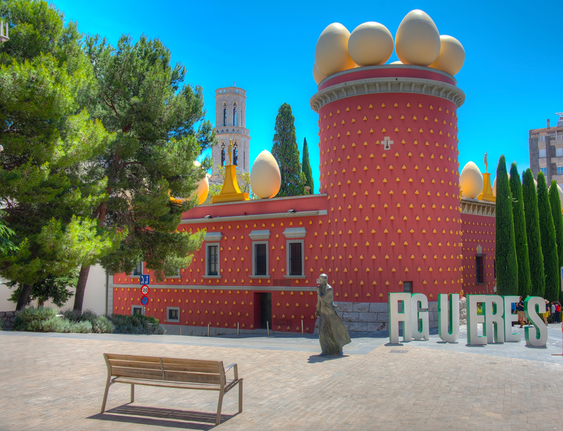 Exterior view of red building with egg sculptures and a bell tower in the distance