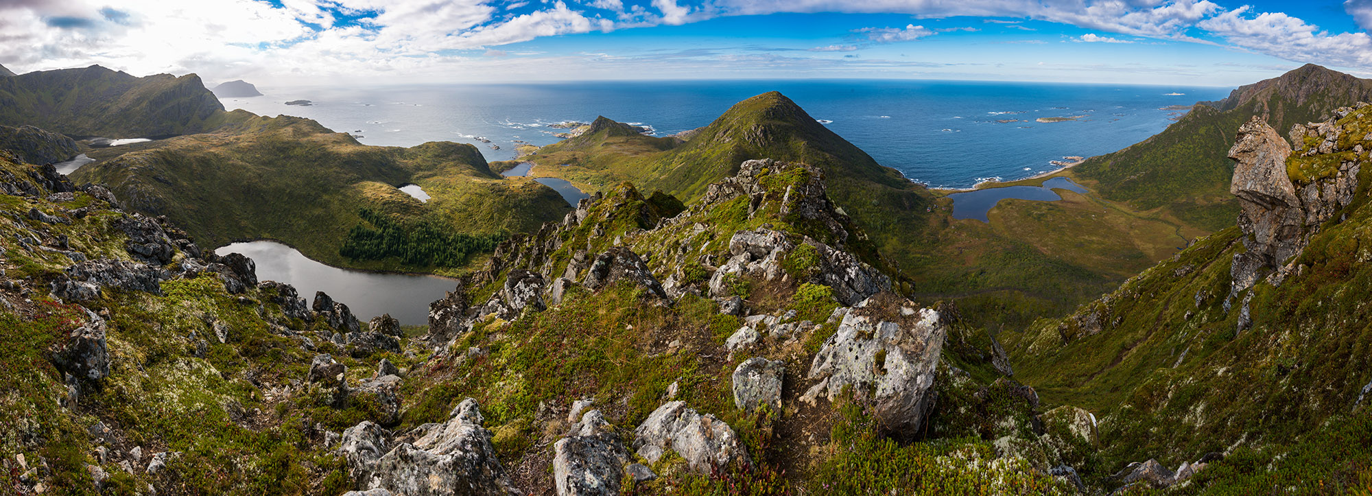 Large, grassy mountains with clouds in the sky and the ocean in the distance