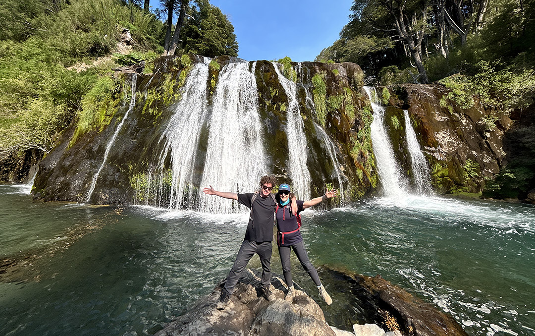 Man and woman with their arms open in front of a waterfall