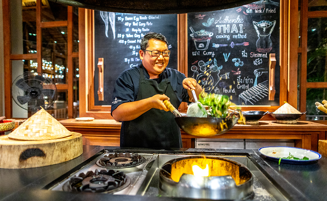 Man cooking with a wok, tossing vegetables over an open flame