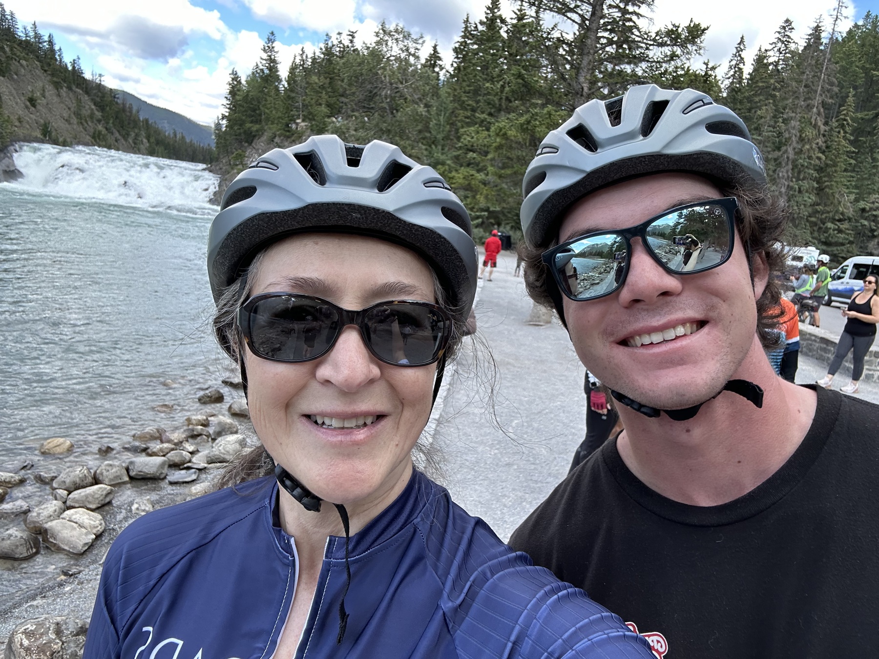 Man and woman wearing biking gear with sunglasses, in front of a large lake