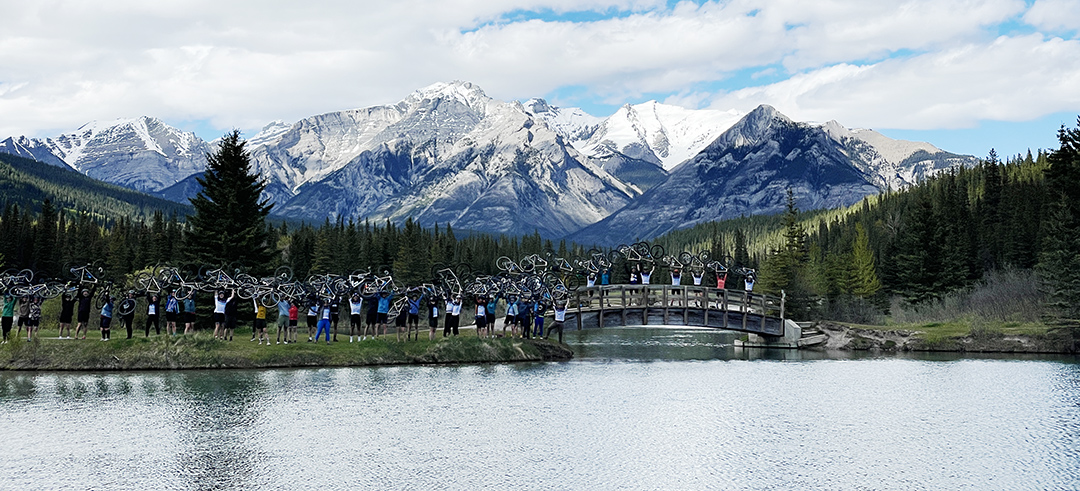 Group of people holding bikes over their head, standing in front of a lake