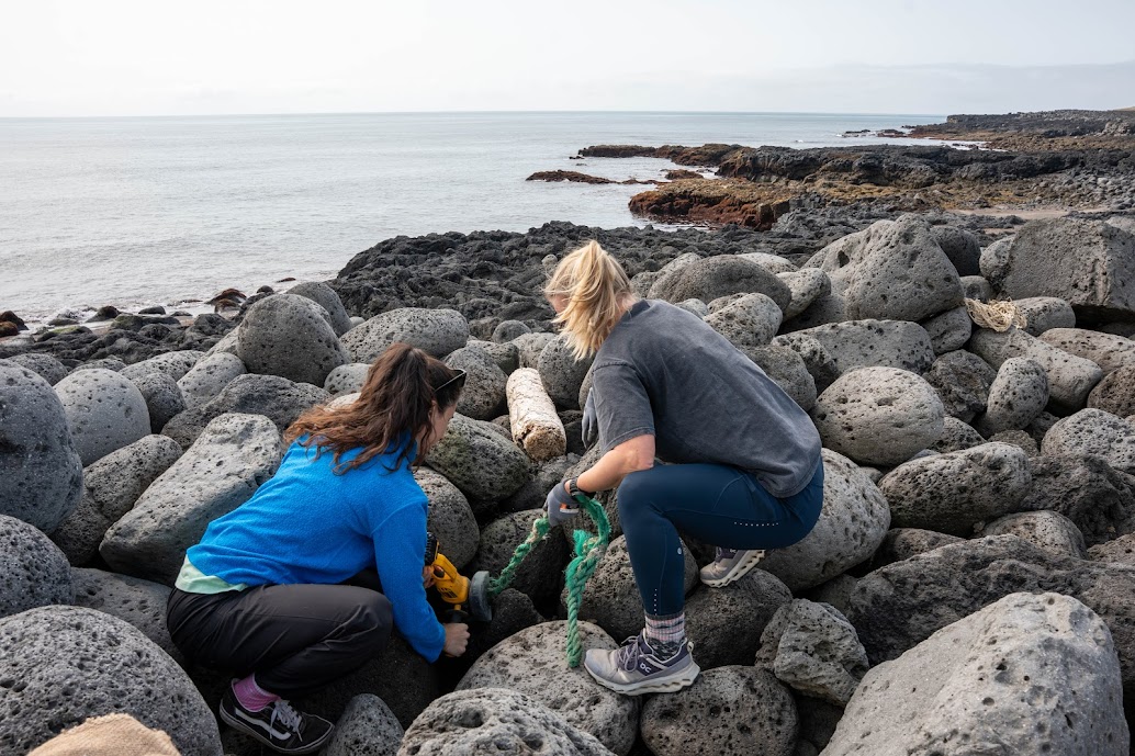 Two women kneeling on large rocks by the ocean