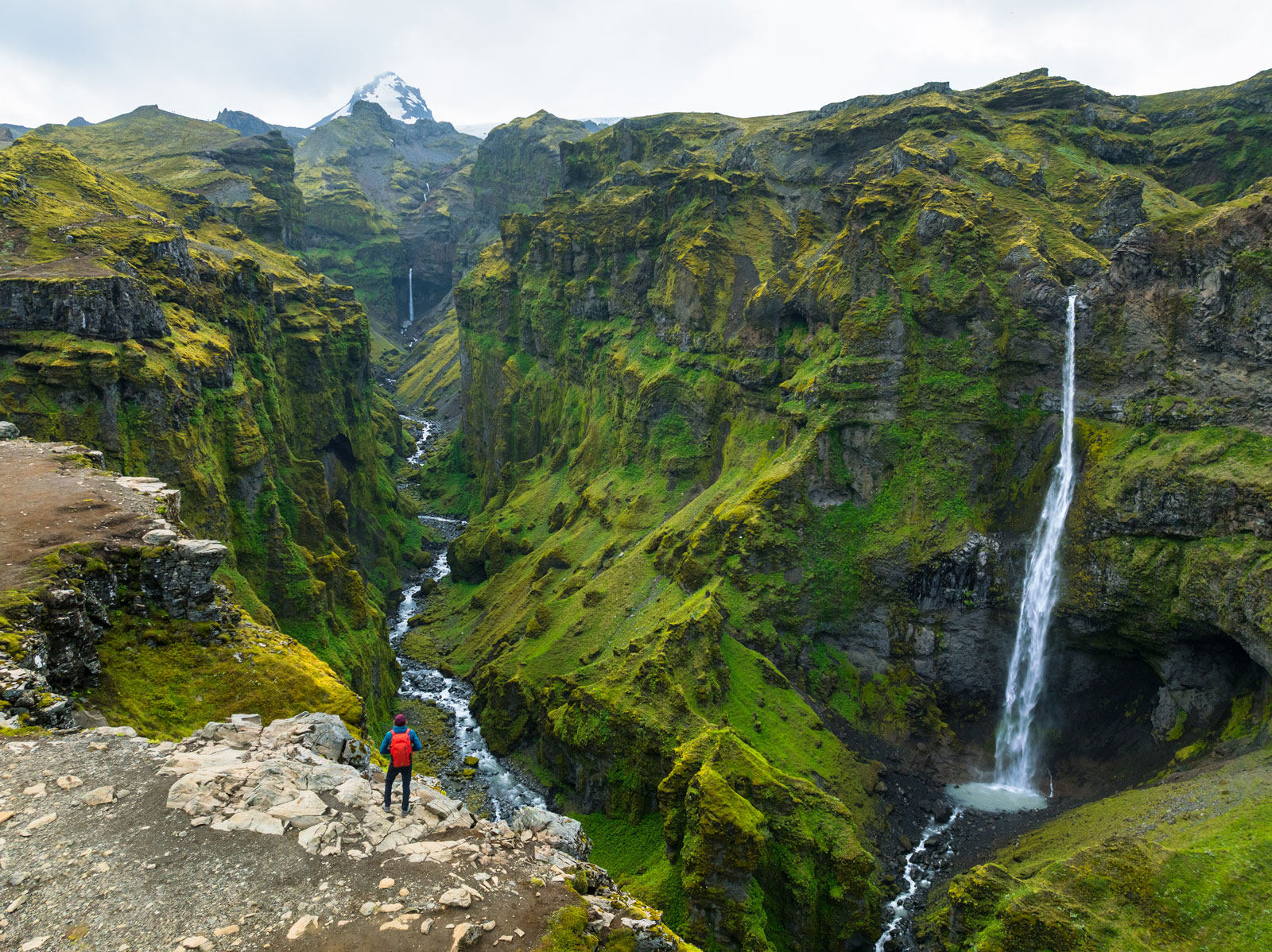 Person standing on a cliff looking down to a valley with a waterfall to the left