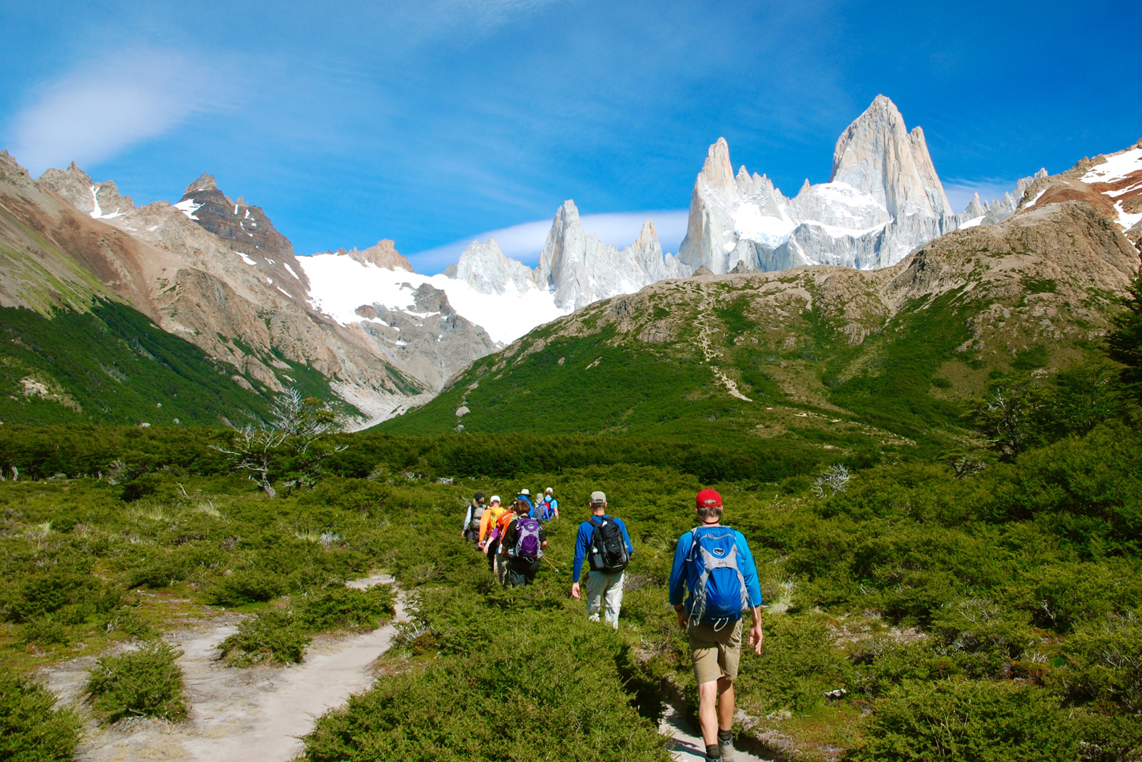 Group of people hiking on a grassy valley with snowy mountains in the distance
