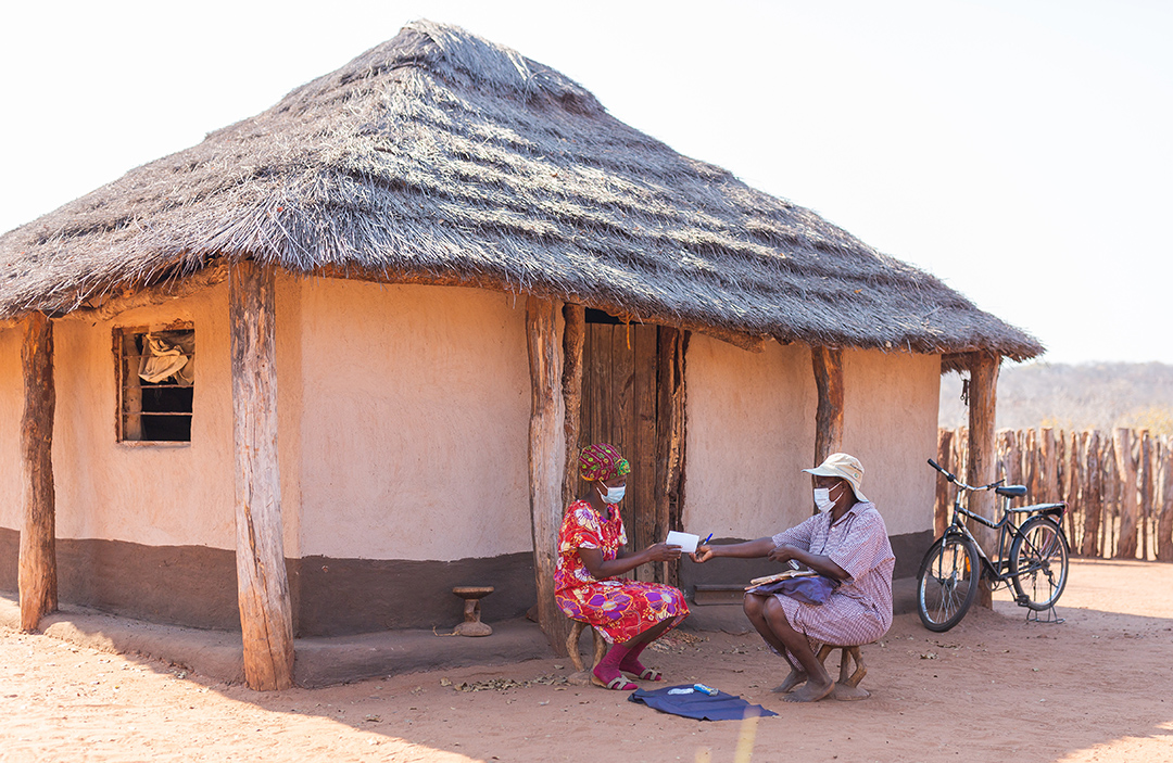 Two women sitting in front of an orange house, with a bicycle in the background