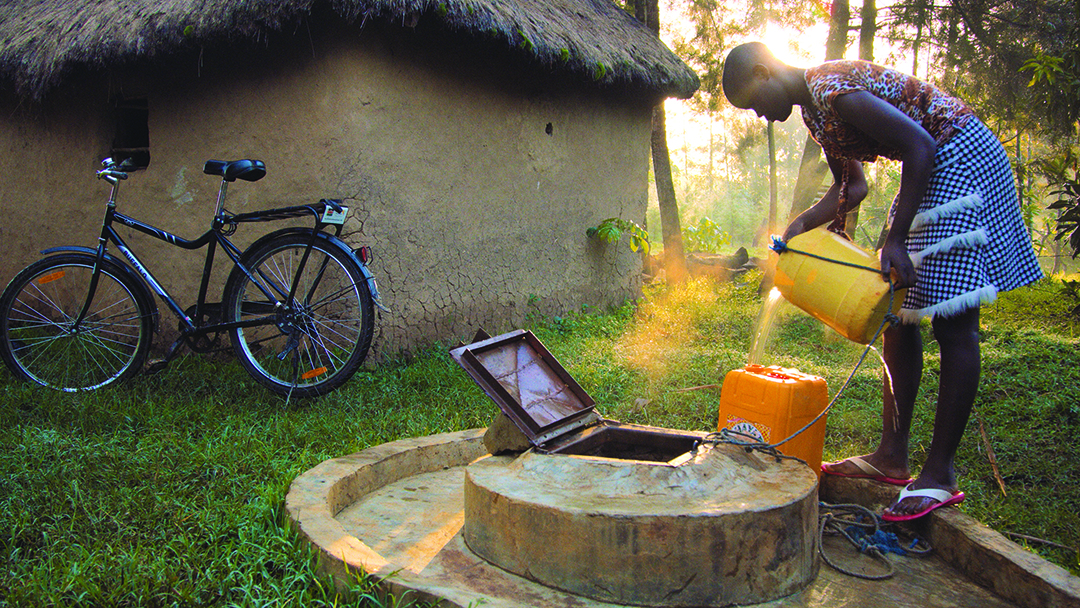 Person collecting water from a well with a bike in the background