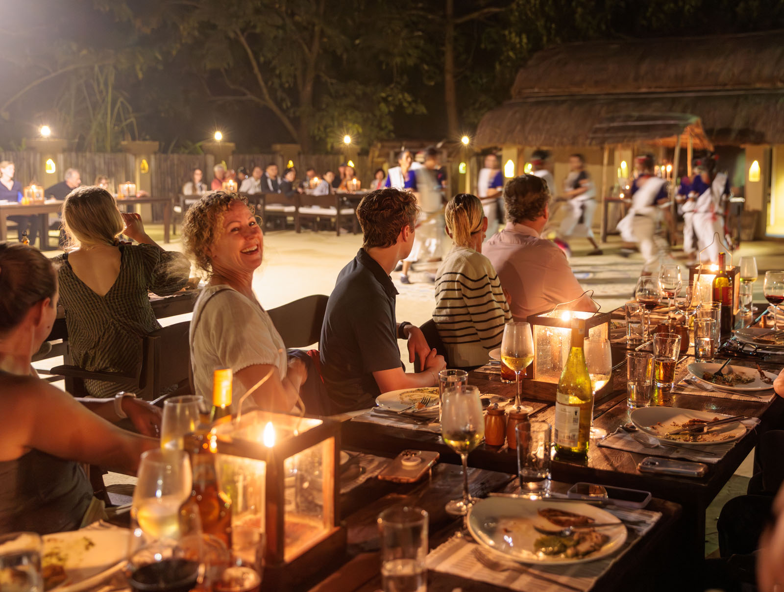 Group of men and women smiling while sitting at dining tables outdoors