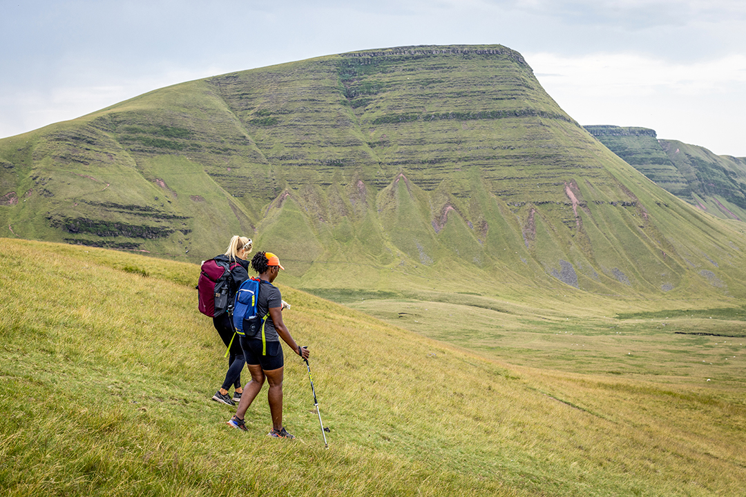 Two women hiking down a grassy hill in a valley